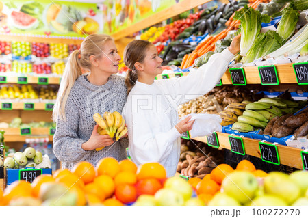 Smiling teenage girl with mother choosing fruits and vegetables in supermarket Smiling teenage girl with mother choosing fruits and vegetables in supermarket 100272270