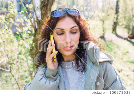 Young brunette woman talking on the phone in spring in the park 100273632