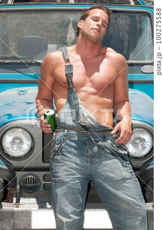attractive athletic young man leaning on his car drinking beer 100275588