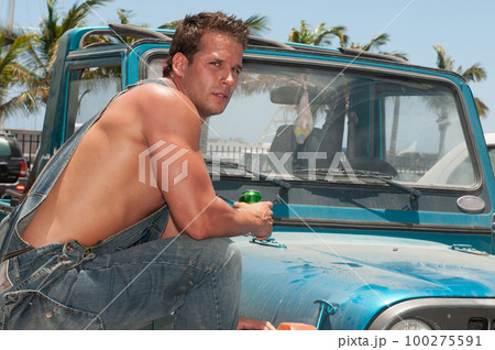 attractive athletic young man leaning on his car drinking beer attractive athletic young man leaning on his car drinking beer 100275591