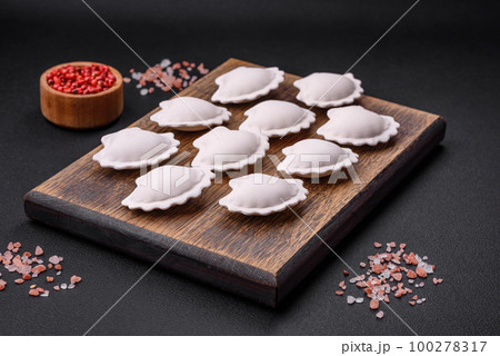 Raw frozen stuffed dumplings on a wooden cutting board 100278317
