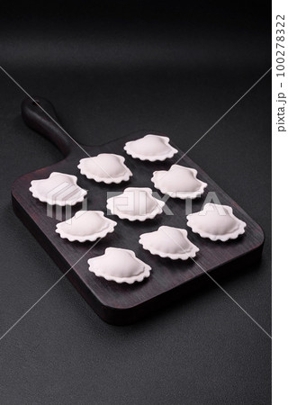 Raw frozen stuffed dumplings on a wooden cutting board 100278322