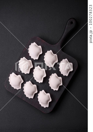 Raw frozen stuffed dumplings on a wooden cutting board 100278323