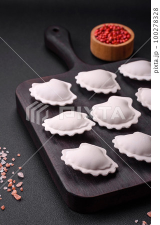 Raw frozen stuffed dumplings on a wooden cutting board 100278328