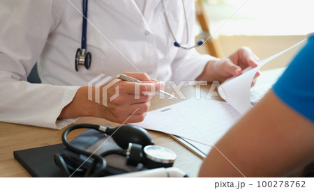 Doctor makes notes in document, sitting at table with patient. Doctor makes notes in document, sitting at table with patient. 100278762
