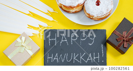 Happy Hanukkah. Jewish dessert Sufganiyot on yellow background. Symbols of religious Judaism holiday. Donuts, candles and gift. 100282561