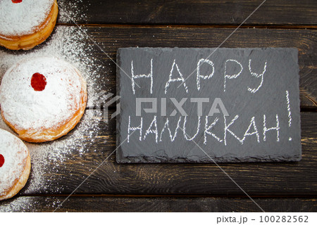 Happy Hanukkah. Traditional dessert Sufganiyot on dark wooden background. Donuts, candles and gifts. Celebrating Jewish holiday. 100282562