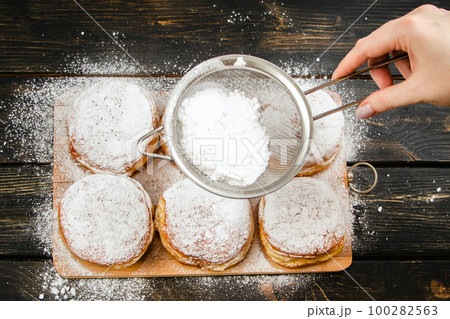 Cooking traditional Hanukkah sufganiyot. Woman sprinkles donuts with powdered sugar. 100282563