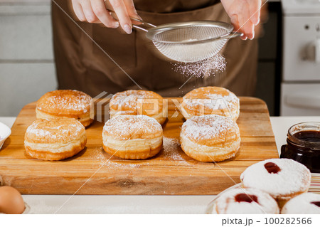 Woman chef prepares fresh donuts in her bakery. Cooking traditional Jewish Hanukkah Sufganiyot. Small business concept. 100282566