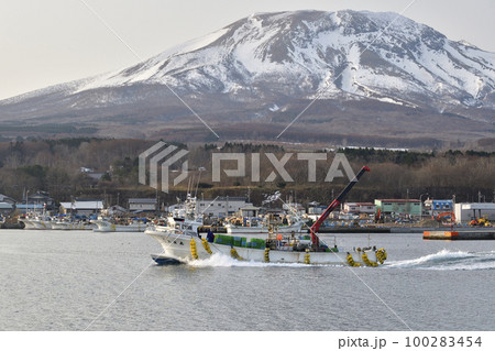 早春の北海道森町砂原漁港を出漁する漁船と残雪の砂原岳の風景を撮影 100283454