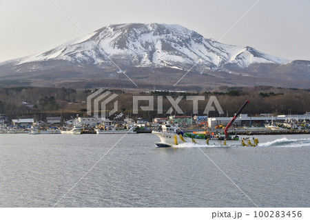 早春の北海道森町砂原漁港を出漁する漁船と残雪の砂原岳の風景を撮影 100283456