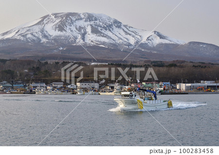 早春の北海道森町砂原漁港を出漁する漁船と残雪の砂原岳の風景を撮影 100283458