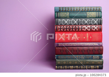 Stack of hardcover books on violet background. Space for text 100284373