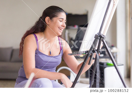 Painting at home, weekend leisure hobby. Happy smiling south american venezuelan middle aged woman 100288152