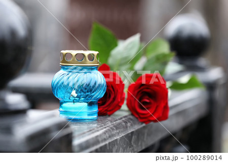 Red roses and candle on black marble tombstone outdoors. Funeral ceremony 100289014