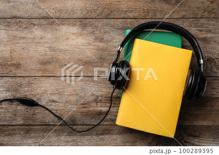 Books and modern headphones on wooden background, top view. Space for text 100289395