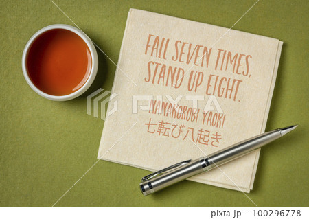 Fall seven times, stand up eight. Japanese proverb on napkin with a cup of tea. Determination and persistence concept. Fall seven times, stand up eight. Japanese proverb on napkin with a cup of tea. Determination and persistence concept. 100296778