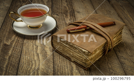 antique leatherbound journal with a cup of tea and pen on a rustic wooden table antique leatherbound journal with a cup of tea and pen on a rustic wooden table 100296795