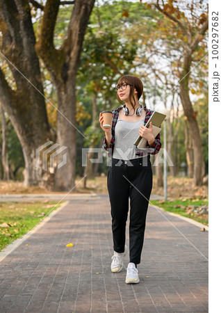 Chilling Asian female college student sipping coffee while walking in the campus park 100297682