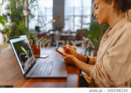 Florist woman works in her small floral business surf for information about plants using laptop Florist woman works in her small floral business surf for information about plants using laptop 100298230