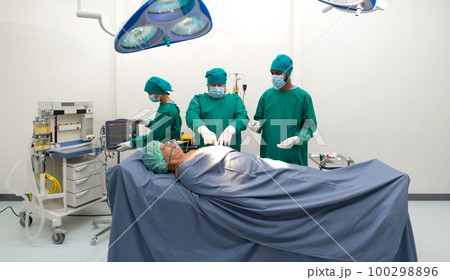 Group of surgeons and nurse in surgical green gown uniform performing surgical operation in operating room. 100298896