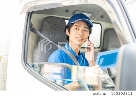 運転席でスマホを使う若い男性ドライバー 100302311