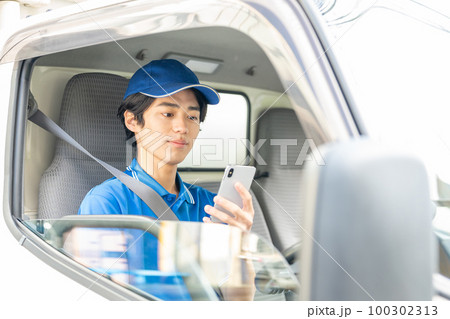 運転席でスマホを使う若い男性ドライバー 100302313
