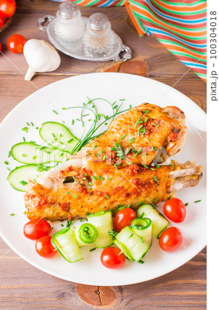 Baked in a spices turkey wing, cucumber slices and cherry tomatoes on a plate on a wooden table 100304018