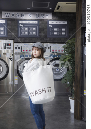 コインランドリーでランドリーバッグを持つ若い女性 100310748