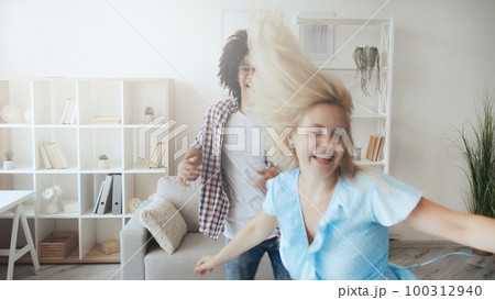 Couple fun. Crazy weekend. Happy moments. Defocused joyful excited girl dancing with boyfriend at light morning home interior with copy space. 100312940