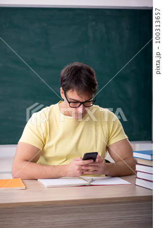 Young male student sitting in front of green board 100313657