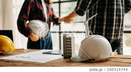Construction team shake hands greeting start new project plan behind yellow helmet on desk in office center to consults about their building project. 100314744