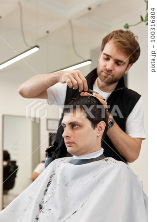 hairdresser does haircut for caucasian bearded man 100316804