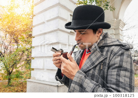 Portrait of a man in a hat smoking a pipe on a city street. Unhealthy Lifestyle 100318125