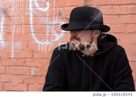 Young man in black clothes smoking a cigarette outdoors against a brick wall. Young man in black clothes smoking a cigarette outdoors against a brick wall. 100319343