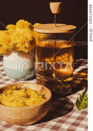 Preparing Dandelion flower healthy tea in glass cup on table. Herbal medicine Delicious tisane tea from with fresh yellow blossom dandelion flowers inside tea cup. Green clearing infusion Wildflowers 100319498
