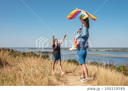 Happy family have fun playing with a kite in nature. The child sits on the shoulders of his father. Happy family have fun playing with a kite in nature. The child sits on the shoulders of his father. 100319589