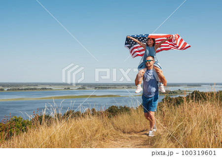 Happy family father and daughter sit on fathers shoulders with america flag in nature on a sunny day. Free lifestyle 100319601