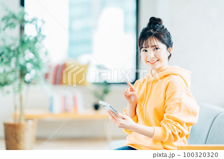 リビングでスマートフォンを操作している大学生。 リビングでスマートフォンを操作している大学生。 100320320