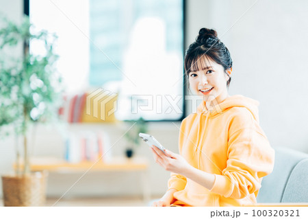 リビングでスマートフォンを操作している大学生。 100320321