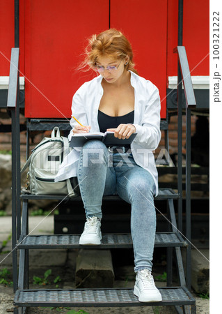 Young attractive woman sitting at the stairs and drawing sketch in the notebook 100321222