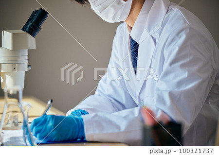 実験データをメモする白衣の若い男性 100321737
