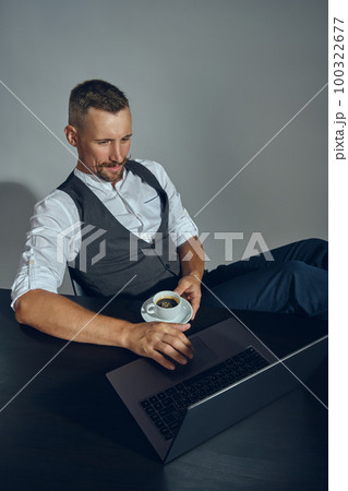 Bearded businessman with stylish mustache, dressed in classic suit is working at laptop while sitting at table in office, gray background. Top view. 100322677
