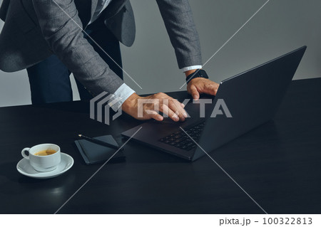 Close-up shot of businessman hands, he is working at a laptop in office, gray background. Dressed in a classic suit and white shirt. 100322813