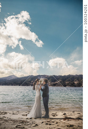 海辺でウエディングフォトを撮っている新婚夫婦 100324201