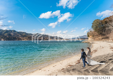 海辺でウエディングフォトを撮っている新婚夫婦 100324243