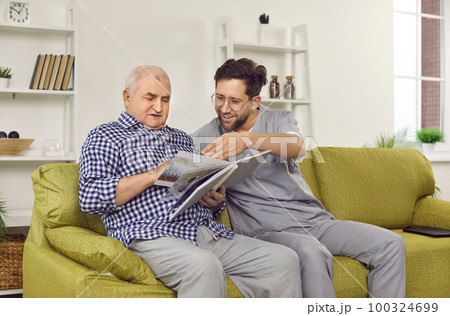 Elderly man and a retirement home worker looking through a book or photo album together Elderly man and a retirement home worker looking through a book or photo album together 100324699