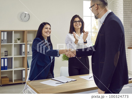 Handsome gray-haired businessman with glasses shakes hands with attractive brunette with long hair as sign of concluding good business deal. Handsome gray-haired businessman with glasses shakes hands with attractive brunette with long hair as sign of concluding good business deal. 100324773
