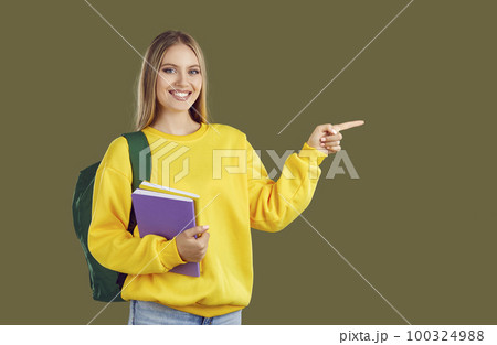 Happy student girl with backpack and copybooks pointing finger on copy space on khaki background. 100324988