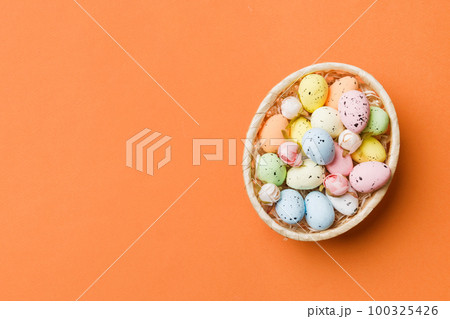 Colorful Easter eggs in wicker basket against colored background, closeup. top view with copy space Colorful Easter eggs in wicker basket against colored background, closeup. top view with copy space 100325426